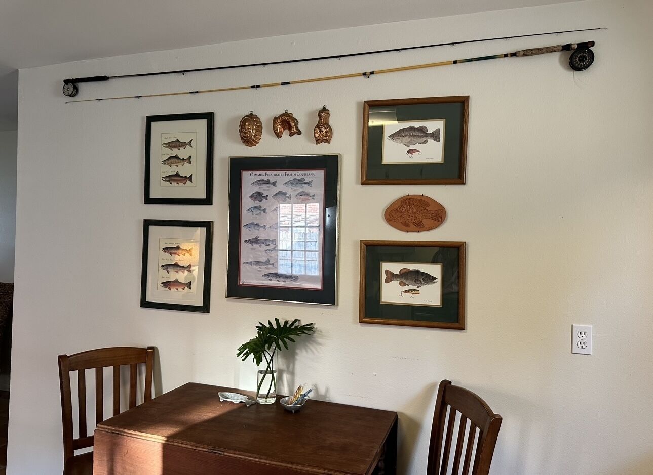 A dining area with a wooden table and chairs, framed fish illustrations on the wall, and a fishing rod.