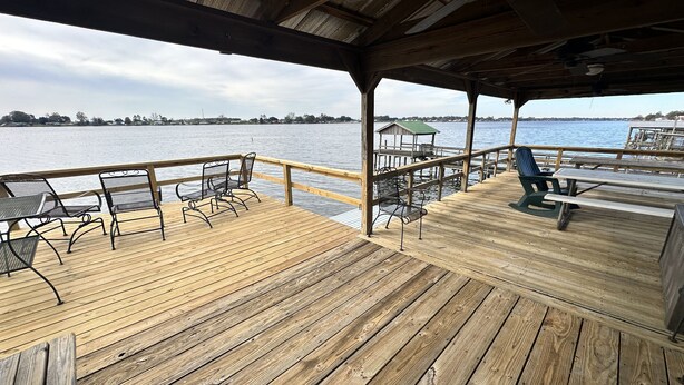 A wooden deck with metal chairs and tables overlooking a body of water.