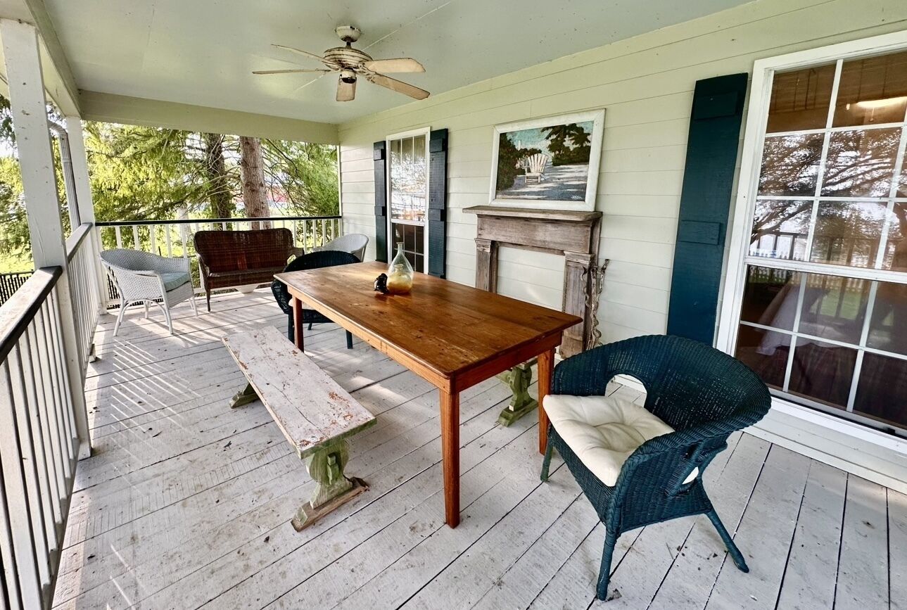 Une véranda couverte avec une table et des chaises en bois, une cheminée et un ventilateur de plafond.