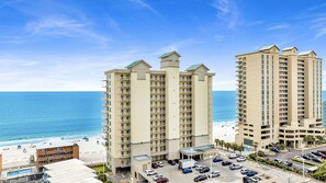 A high-rise hotel with multiple balconies, a swimming pool, and a beach view.