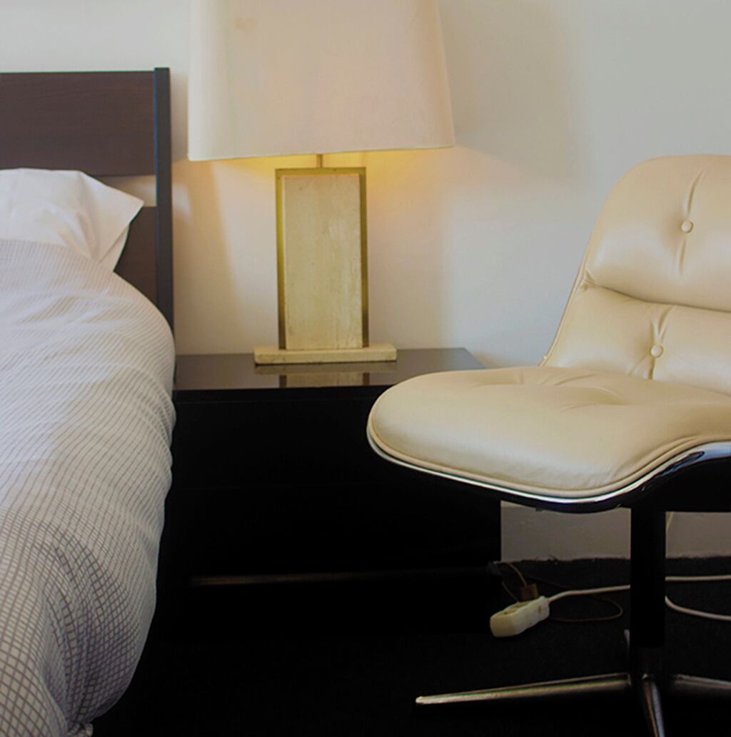 Et hotelværelse med en seng, et natbord med en lampe og en stol.
