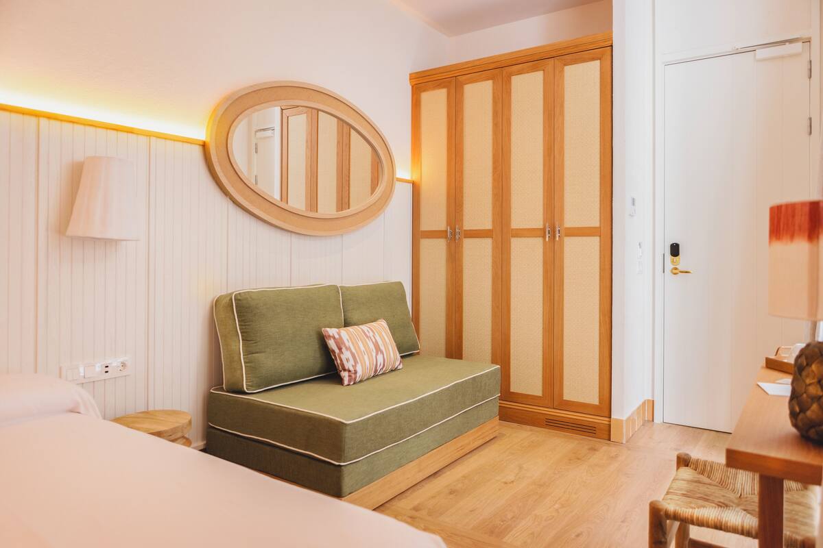 Ein Hotelzimmer mit einem grünen Sofa, einem Holzschrank, einem runden Spiegel und einem Holztisch.