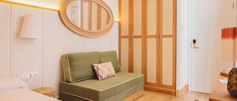 A hotel room with a green sofa, a wooden wardrobe, a round mirror, and a wooden dining table.