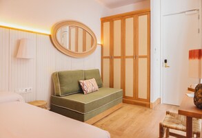 Habitación de hotel con sofá verde, armario de madera, espejo redondo y mesa de comedor de madera.