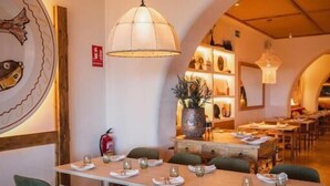 Un restaurant avec un sol à carreaux, des chaises recouvertes d’un tissu vert et une grande table à manger placée au centre de la salle, prête pour le repas.