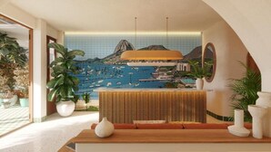 Un espace d’accueil agrémenté d’une fresque représentant une ville côtière, d’un comptoir de réception en bois et de plantes en pot.