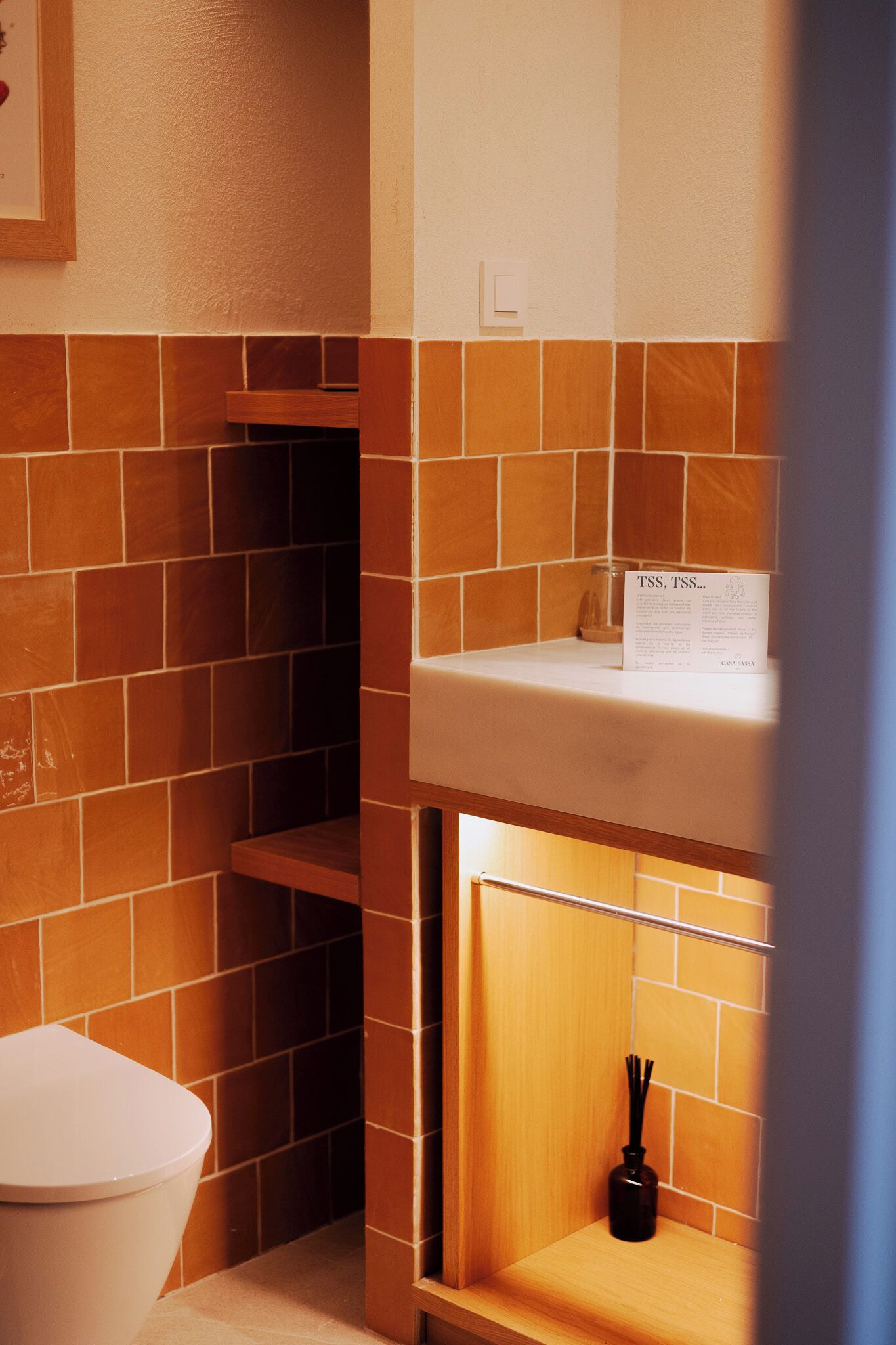 Ein Badezimmer mit einer weißen Toilette, einem Regal mit einem Schild und einer Flasche zur Raumduftung.