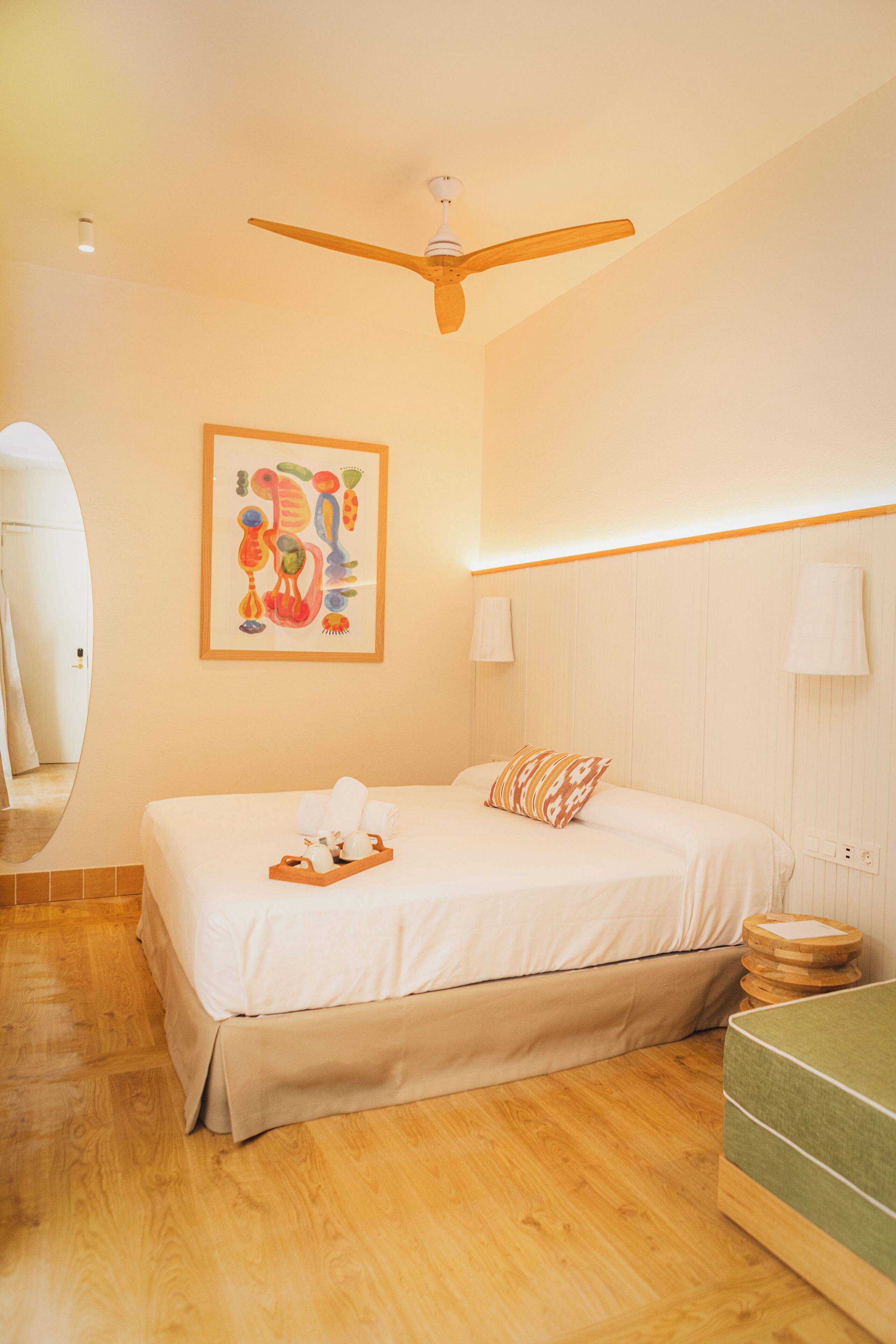 Een hotelkamer met een bed, een plafondventilator, een aan de muur bevestigde lamp en een houten nachtkastje.