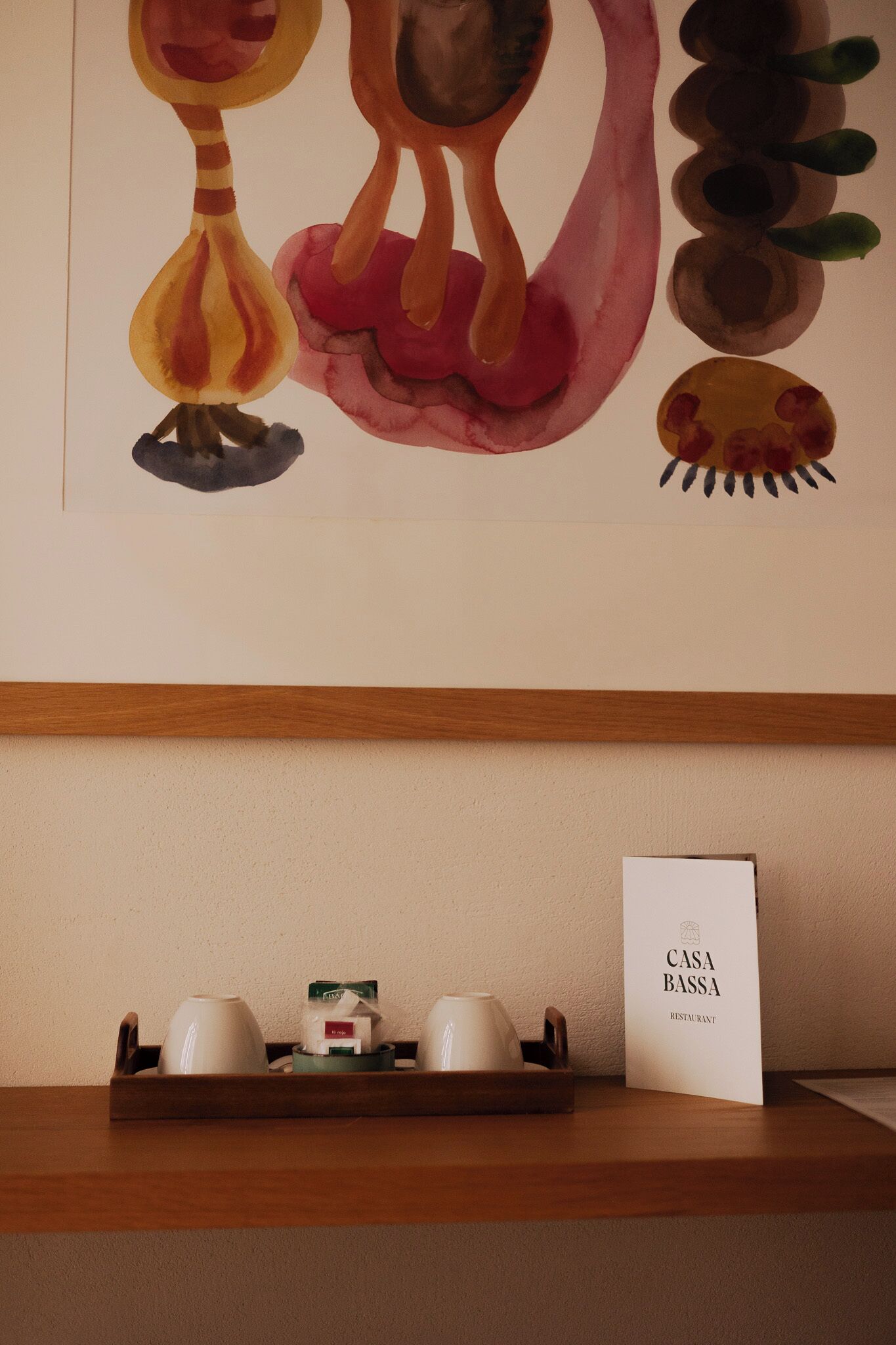 Una pared con arte abstracto, una bandeja con tazas y un menú, y una estanter ía de madera.