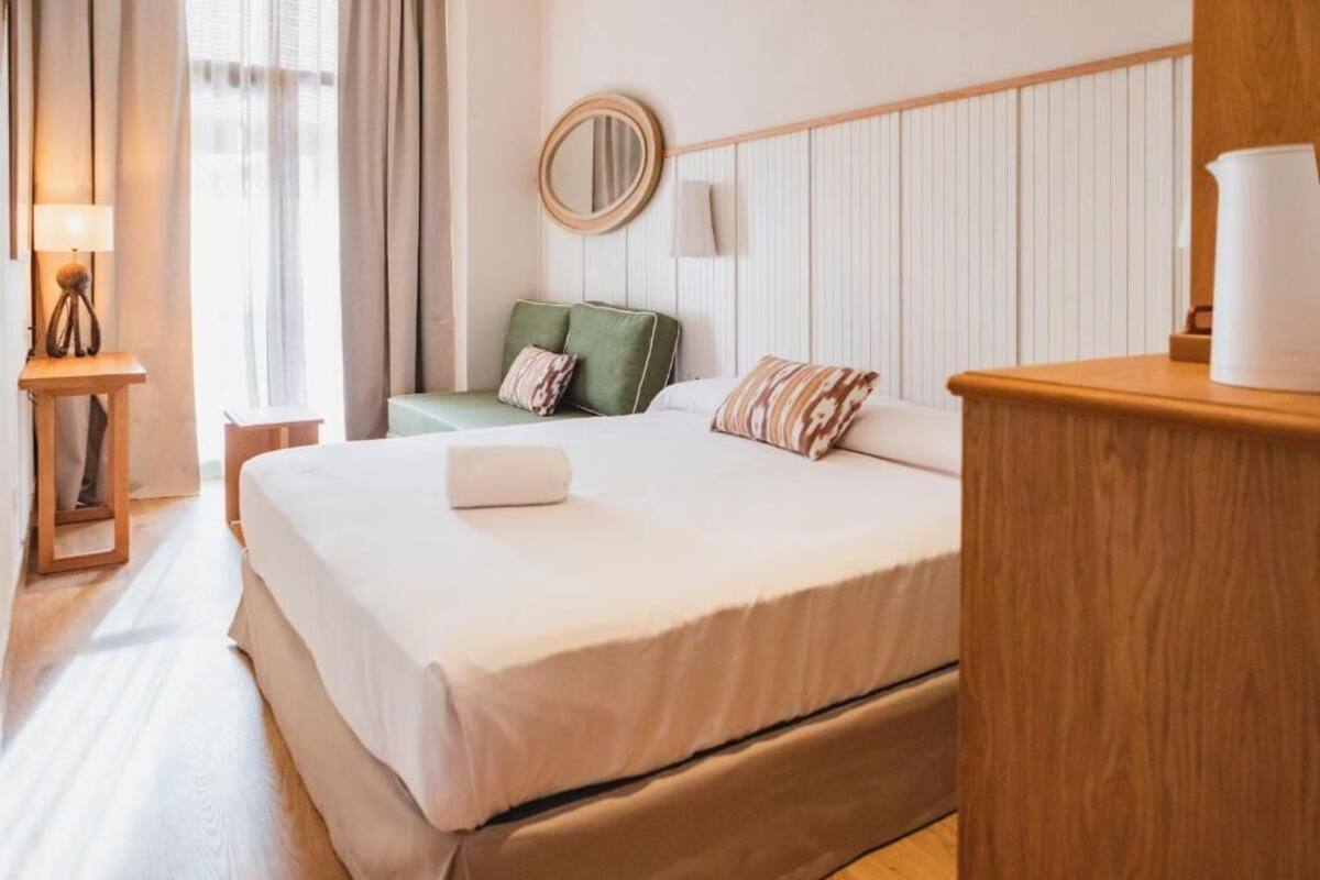 Ein Hotelzimmer mit einem großen Bett, einem Nachttisch mit Lampe, einem grünen Sessel und einem Holzbeistelltisch.