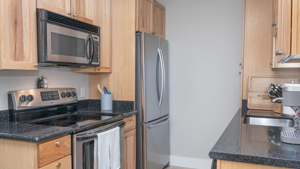 A modern kitchen with stainless steel appliances, wooden cabinets, and a granite countertop.