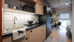 A modern kitchen with wooden cabinets, a black refrigerator, and a microwave. There is a sink with a faucet and a bowl on the counter. - MILESTONE Wroclaw Fabryczna by Tribera (Wroclaw)