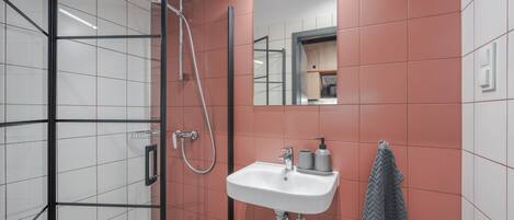 Une salle de bain avec une douche à parois de verre, un lavabo blanc avec un miroir au-dessus, et une serviette accrochée au mur.