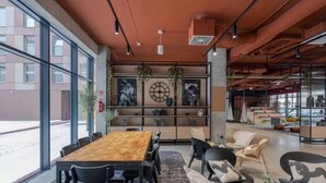 A modern interior with a wooden table and chairs, a bookshelf, and a large window overlooking a snowy street. - MILESTONE Wroclaw Fabryczna by Tribera (Wroclaw)