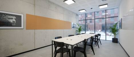 Un salón de conferencias con una larga mesa, sillas negras y ventanas amplias que ofrecen vistas a edificios.