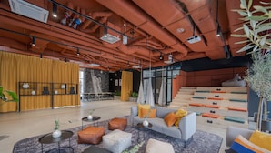 A modern interior with a seating area featuring sofas and ottomans, a staircase, and a bar area with a yellow curtain. - MILESTONE Wroclaw Fabryczna by Tribera (Wroclaw)