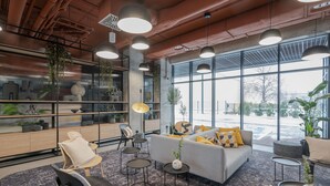 A modern interior with a sofa, chairs, and a coffee table. There are large windows and a view of the outdoors. - MILESTONE Wroclaw Fabryczna by Tribera (Wroclaw)