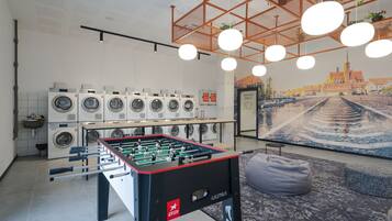 A modern indoor space with a foosball table, multiple washing machines, and a mural of a cityscape.