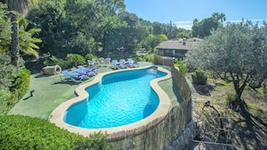 Piscina cercada por vegetação e uma casa ao fundo, com uma cerca de madeira.