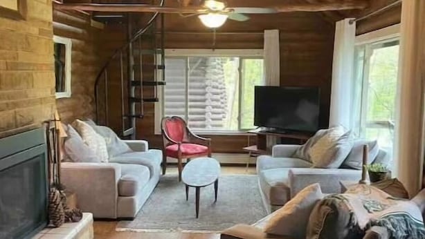 A cozy living room with a fireplace, two sofas, a TV, and a staircase leading to upper floors.