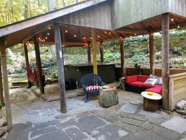 An outdoor patio area with stone flooring, wooden furniture, and string lights.