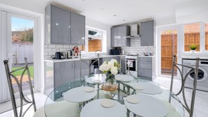 A modern kitchen with grey cabinets, a glass dining table, and a view of the garden. - 3 Bedroom House with Parking in Windsor (Windsor)