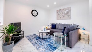 A modern living room with a grey sofa, a round coffee table, a TV on a black stand, a potted plant, and a blue patterned rug. - 3 Bedroom House with Parking in Windsor (Windsor)