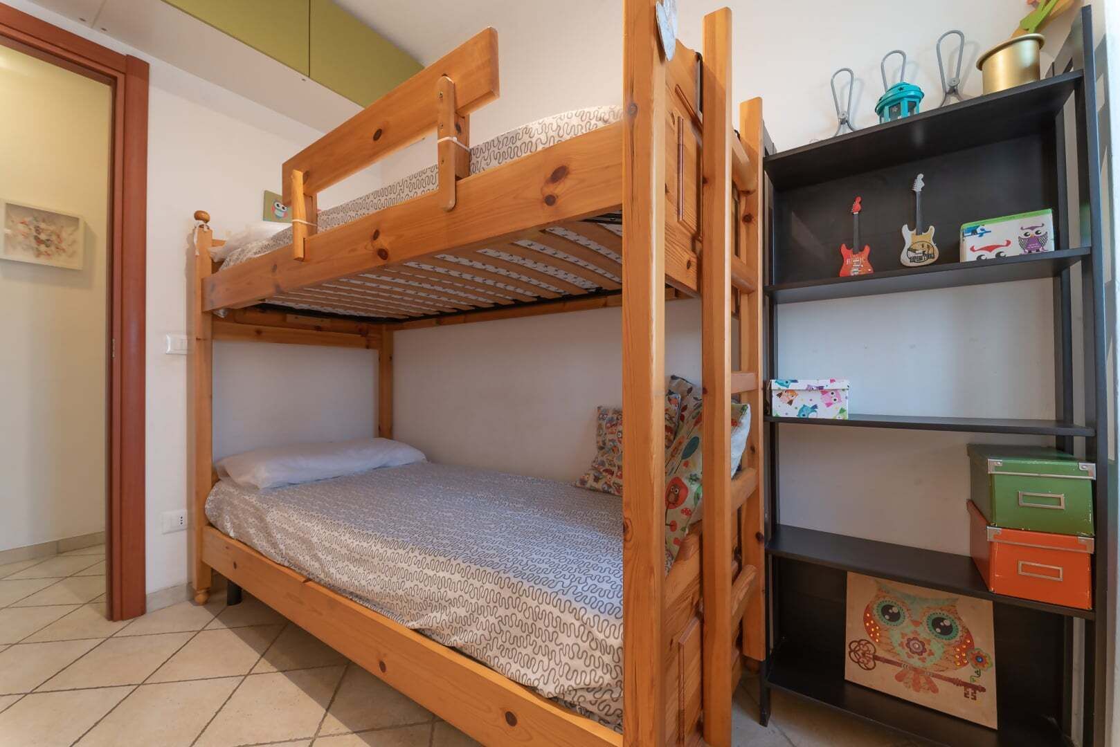 Un lit superposé avec une structure en bois, une étagère avec des boîtes de rangement et une étagère murale agrémentée d’objets décoratifs.
