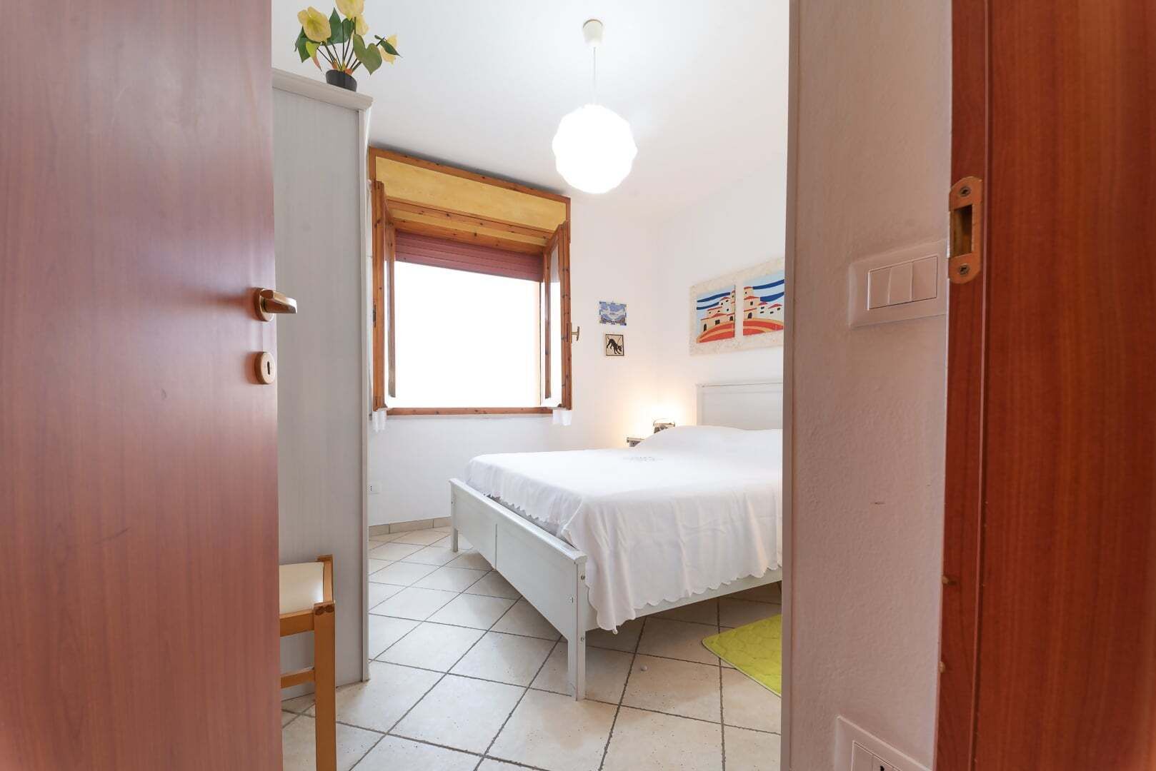 A bedroom with a bed, a window with curtains, a bedside table, and a wall-mounted light fixture.