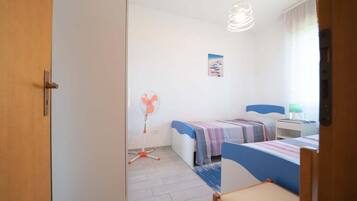 Une chambre avec deux lits, un ventilateur, une lampe et un tableau accroché au mur.