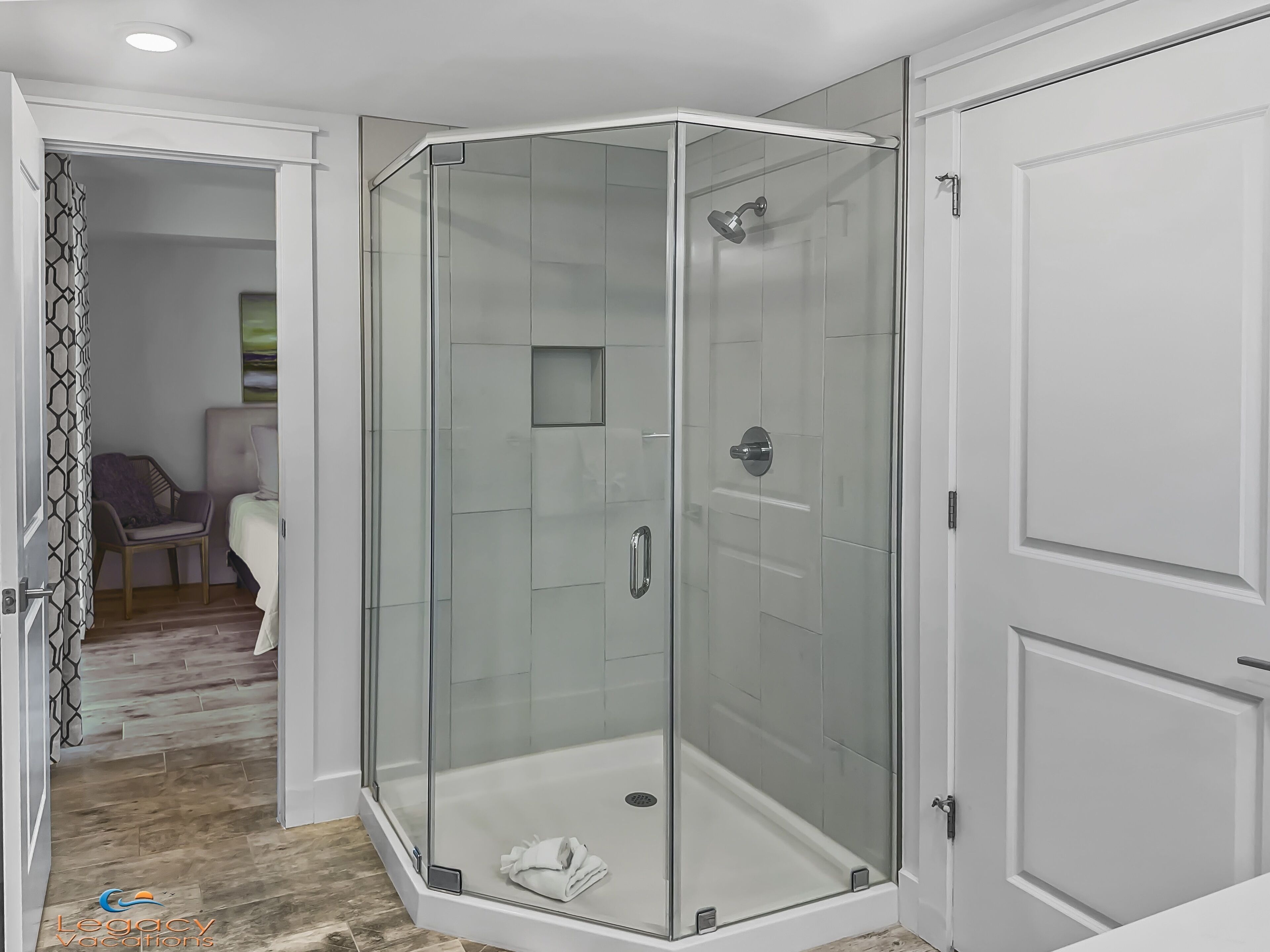 A modern bathroom with a glass-enclosed shower, a white door, and a visible towel on the floor.