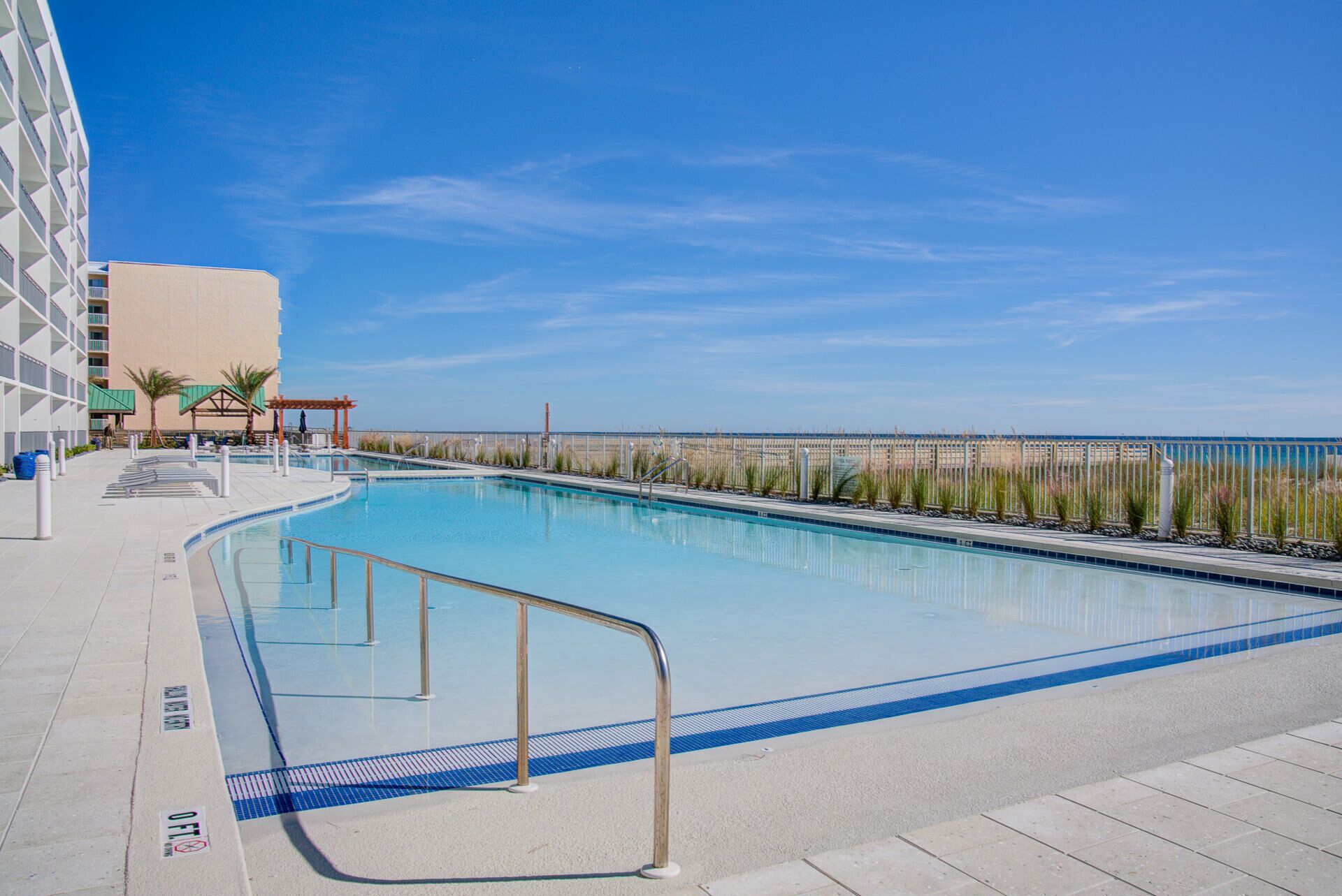 Piscina com vista clara para o oceano, área de estar coberta e edifício com design moderno.