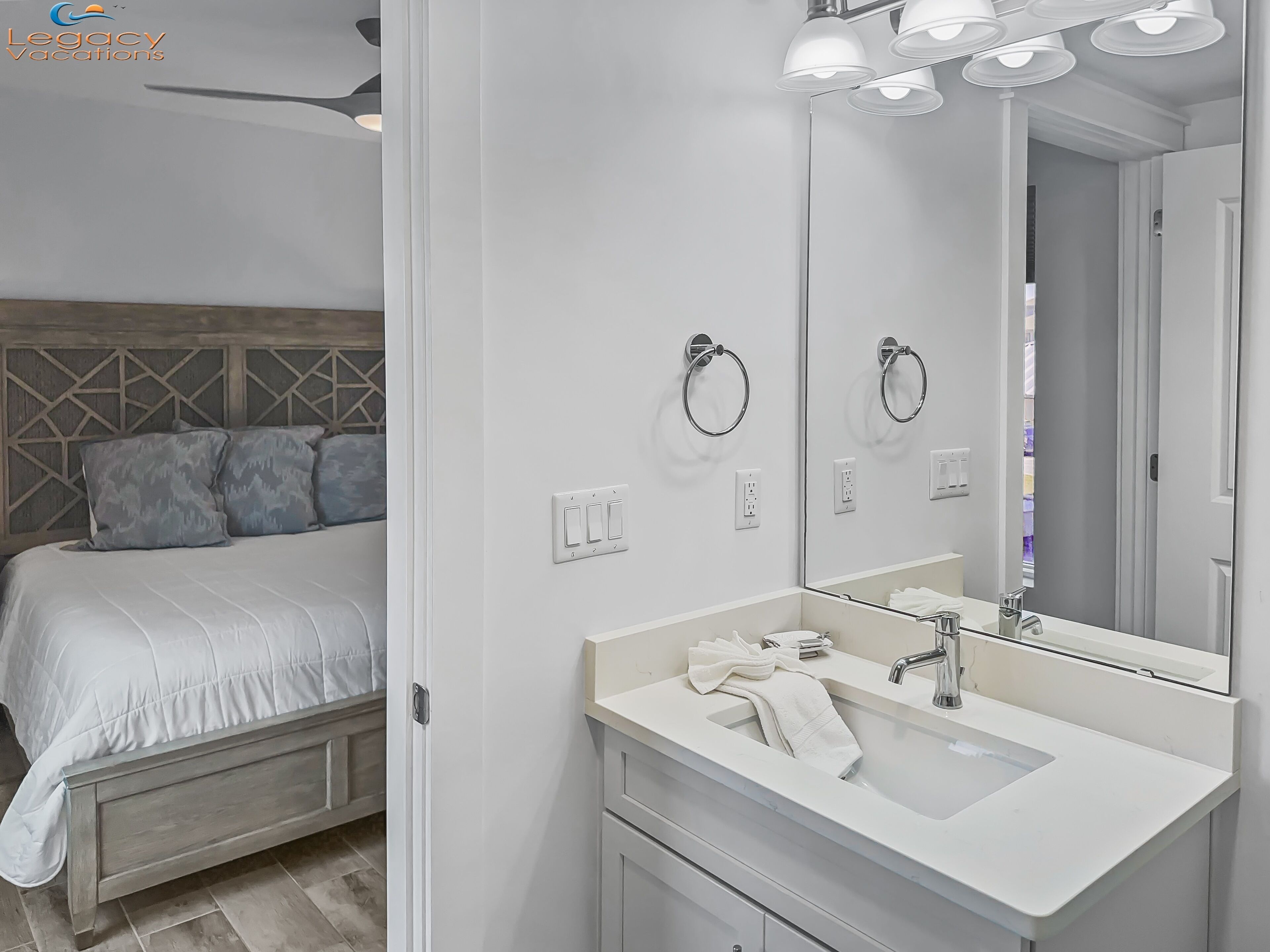 A modern bedroom with a bed, bedside table, and a large mirror above the sink.