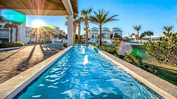 A swimming pool with water fountains, surrounded by palm trees and a clear blue sky. - Blu 200 - Large 4Bd Beachfront - Great Amenities Including Beach Service! (Fort Walton Beach)