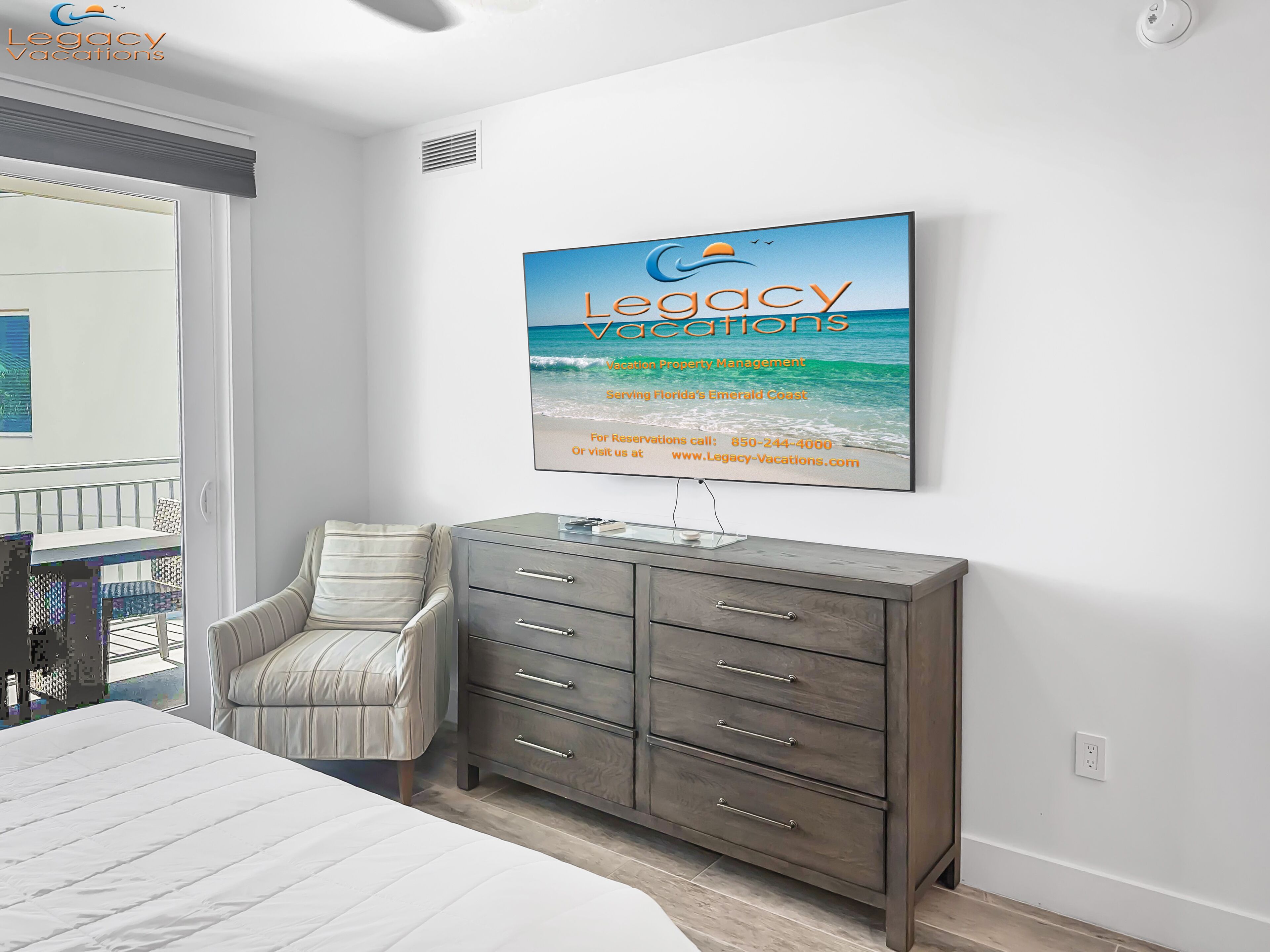 Une chambre à coucher comprenant un lit, une commode grise, une chaise et une œuvre d’art accrochée au mur représentant une scène de plage.