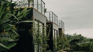 Une maison moderne dotée d’un balcon en verre, entourée d’une végétation luxuriante et agrémentée d’une terrasse en bois.