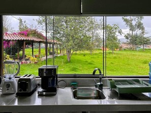 A kitchen with a large window, a blender, a toaster, a coffee maker, a sink, and a dish rack.