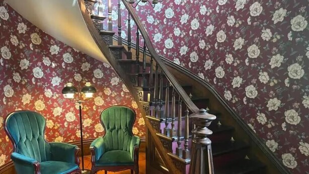 A staircase with floral wallpaper, two green upholstered chairs, and a floor lamp.