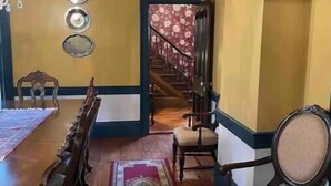 A dining room with a long wooden table, multiple chairs, a red and gold patterned rug, and a staircase leading to another level.