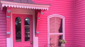 A pink house with a front door, a window, and a small patio with two chairs and a table.