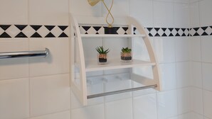 Een badkamer met witte betegelde wanden, een zwart-wit patroonrand, een witte plank met twee plantenpotten, en een gouden decoratief object.