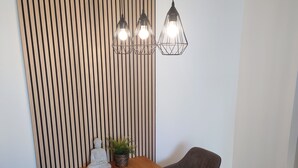 Een eetgedeelte met een houten tafel, zes stoelen, een plant in pot en drie hanglampen.