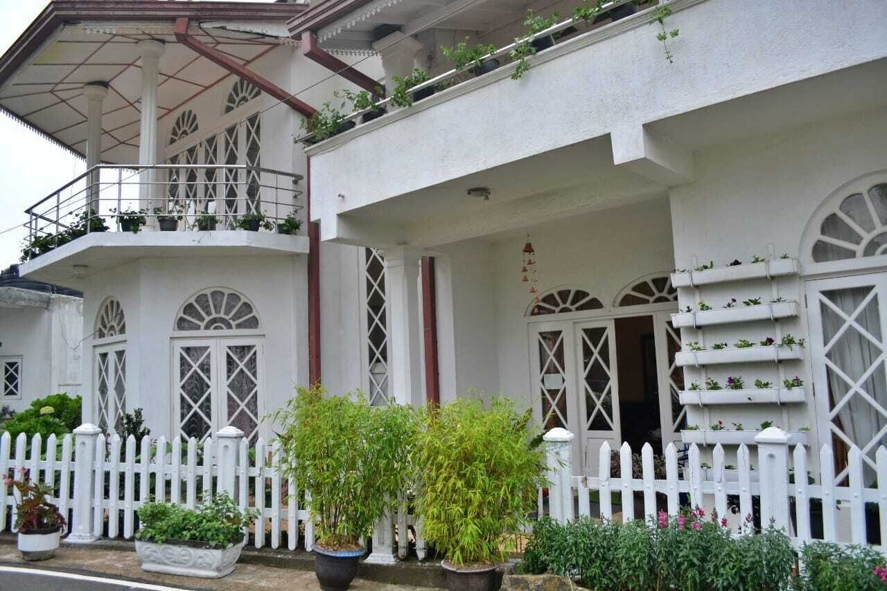 A white building with a balcony, large windows, and a white picket fence.