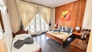 A bedroom with a bed, a bedside table, a nightstand, a window with curtains, and a wooden wall with a painting. - MAPLES HOLIDAY RESORT (Nuwara Eliya)