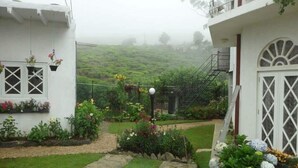 A garden with a stone pathway, potted plants, and a white building with a balcony. - MAPLES HOLIDAY RESORT (Nuwara Eliya)