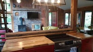 A kitchen with a large island, red cabinets, a stove, and a brick wall. - Red Bend cabin overlooking the river with hot tub. (Bellville)