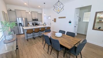 A modern kitchen with stainless steel appliances, a dining area with a wooden table and chairs, and a hanging light fixture.