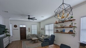 Un salon moderne avec une table à manger en bois, des canapés, un ventilateur de plafond et un luminaire suspendu aux motifs géométriques.