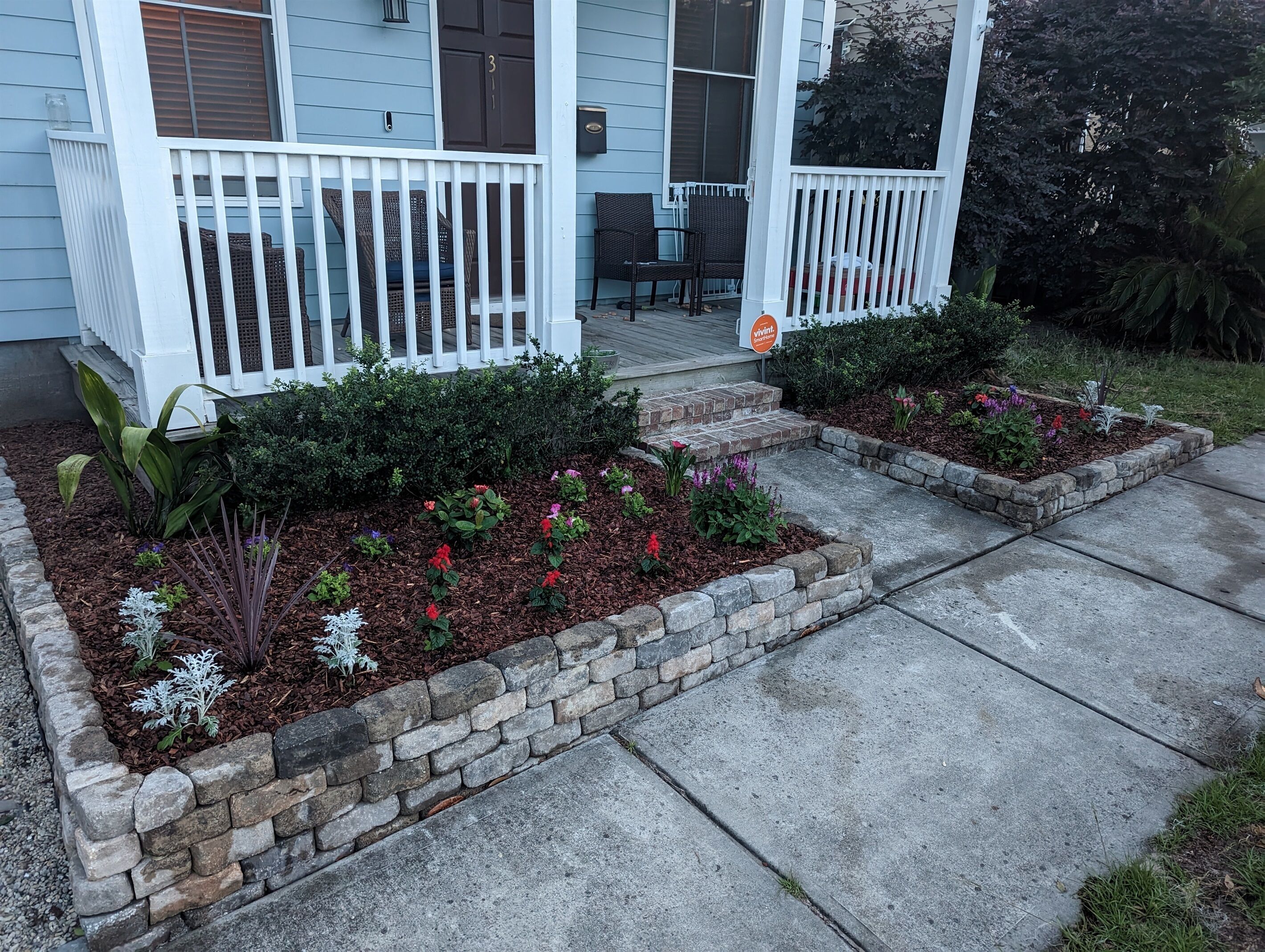 A residential property with a porch, two flower beds, and a mailbox.