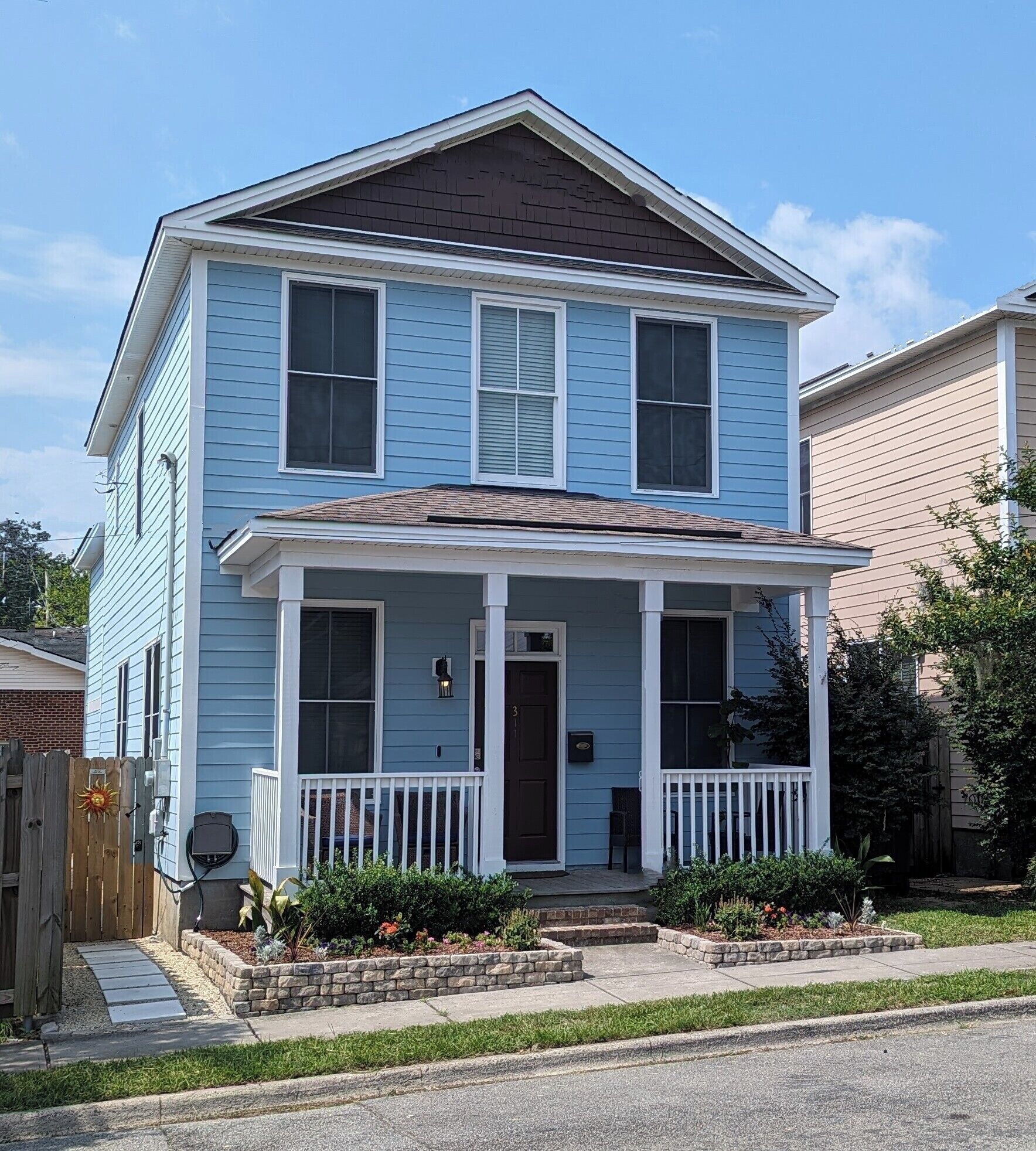A two-story house with a front porch, a mailbox, and a small garden area.